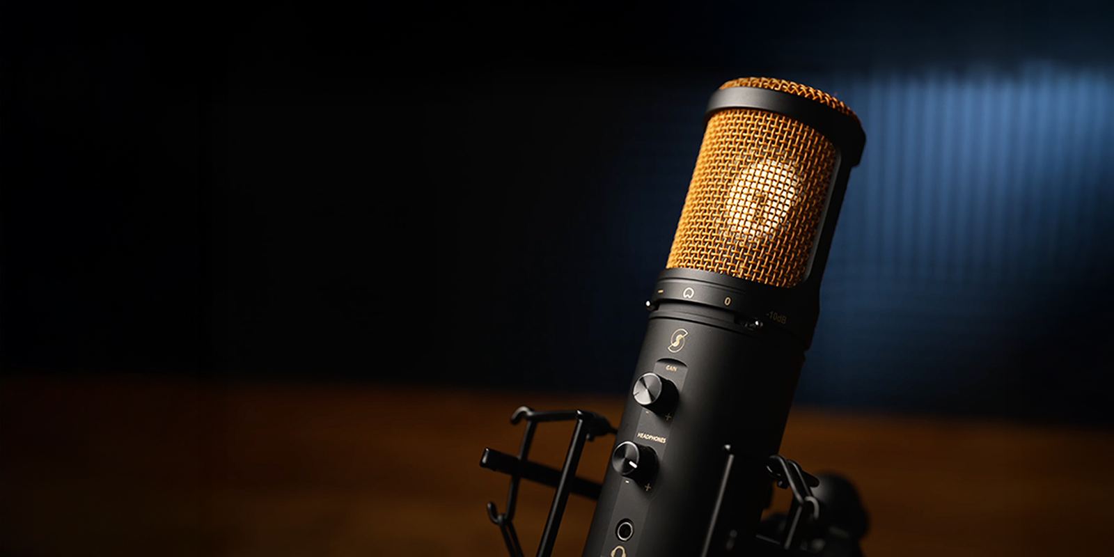 A close-up of a SL600 Editors Keys black studio condenser microphone with a gold mesh grille, mounted on a black stand against a dark background with a blue spotlight.